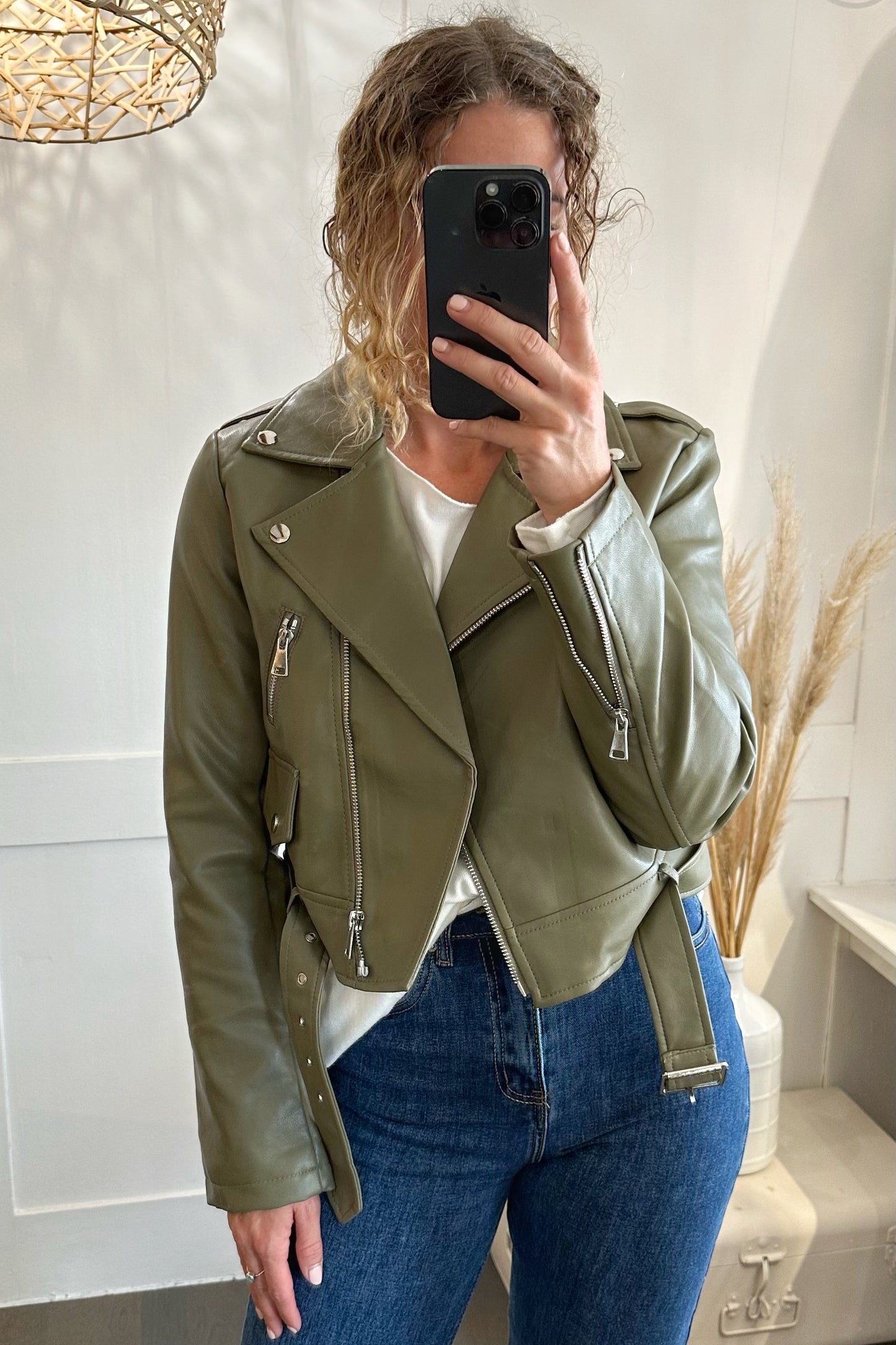 Frau trägt vegane Lederjacke in Eukalyptusgrün mit silbernen Reißverschlüssen und Gürtel, kombiniert mit weißem Shirt und Jeans