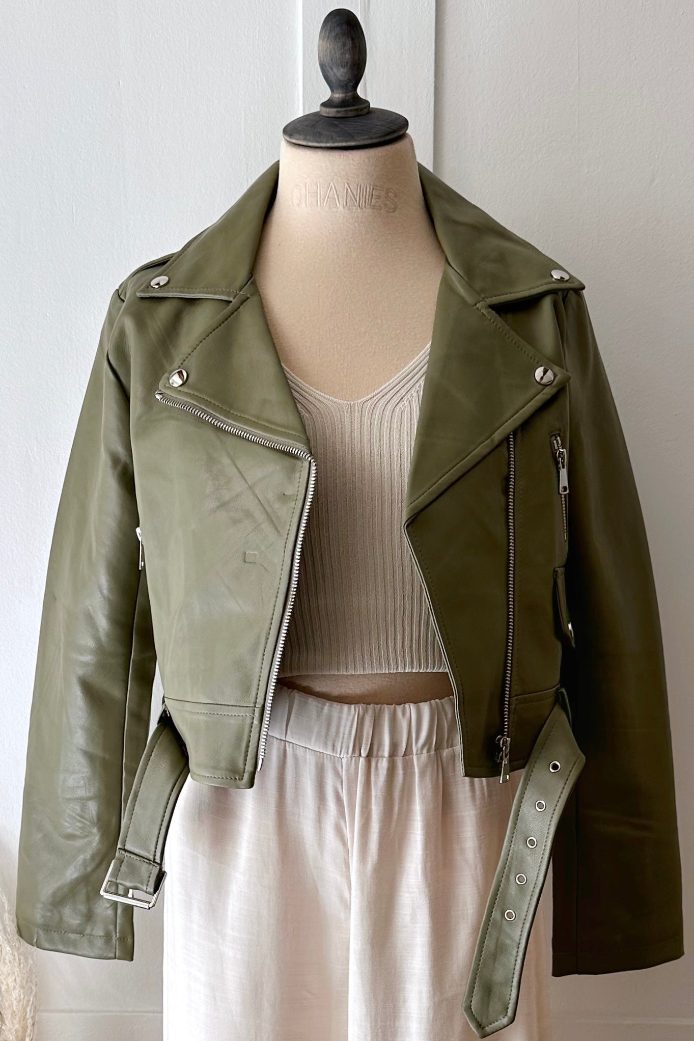 Vegane Lederjacke in Eukalyptusgrün mit silbernen Details, kombiniert mit beigem Stricktop und heller Hose
